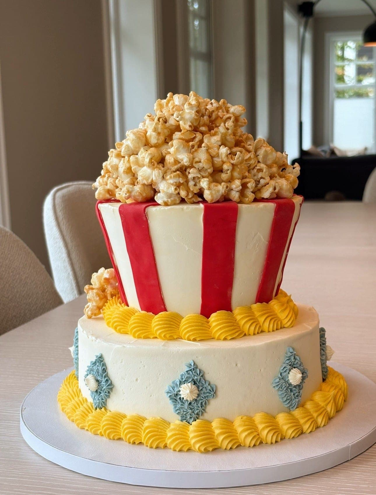 To-etasjes kake formet som en popcornbøtte med røde og hvite striper, toppet med karamellpopcorn og pyntet med gul smørkrempiping